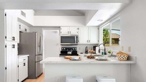 Una cocina moderna con armarios blancos, electrodomésticos de acero inoxidable y una isla central con taburetes.