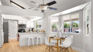 Una cocina moderna con armarios blancos, una isla central y un comedor con mesa de madera y sillas blancas.