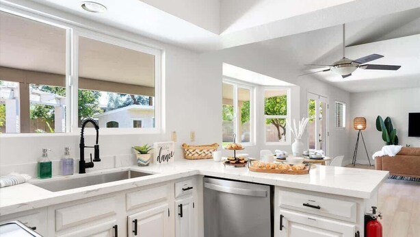 Una cocina moderna con armarios blancos, lavavajillas integrado y un amplio ventanal que proporciona luz natural.