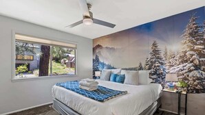 Ein Schlafzimmer mit einem großen Bett, einem Deckenventilator, einem Fenster mit Blick ins Freie und einem Wandbild einer verschneiten Landschaft.