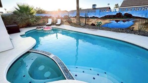 A swimming pool with a hot tub, surrounded by a landscaped area with palm trees and a mural on the wall. - Exclusive retreat- Heated pool & BBQ grill (Peoria)