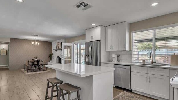A modern kitchen with white cabinetry, stainless steel appliances, and a central island with stools. - Exclusive retreat- Heated pool & BBQ grill (Peoria)