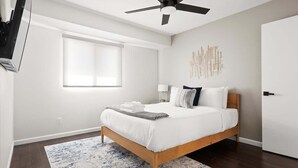 Ein Schlafzimmer mit einem Bett, einem Deckenventilator, einem Fenster und einem an der Wand befestigten Kunstwerk.