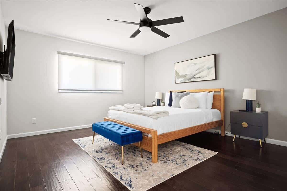 A bedroom with a bed, a ceiling fan, a window, a bedside table, and a nightstand.