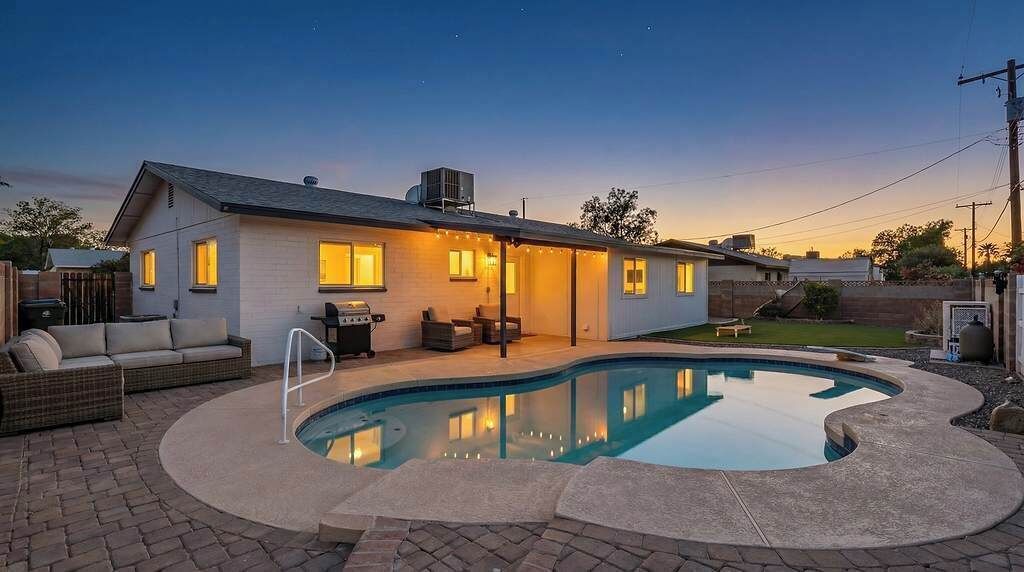 Una casa con piscina, mobiliario exterior y un patio bien iluminado.