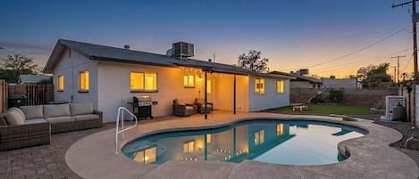 Una casa con piscina, mobiliario exterior y un patio bien iluminado.