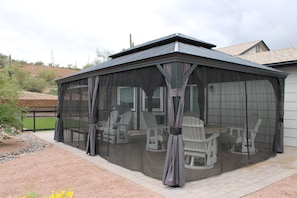 A covered patio area with a table and chairs, a screened enclosure, and a view of a house in the background.