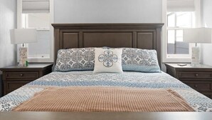Ein Schlafzimmer mit einem großen Bett, zwei Nachttischen, einem Holzkopfbrett, gemusterten Bettbezügen und zwei Nachttischlampen.