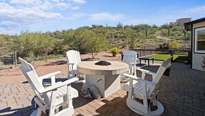 Eine Terrasse mit rundem Tisch und weißen Stühlen, umgeben von einem Backsteinboden und Blick auf eine hügelige Landschaft.