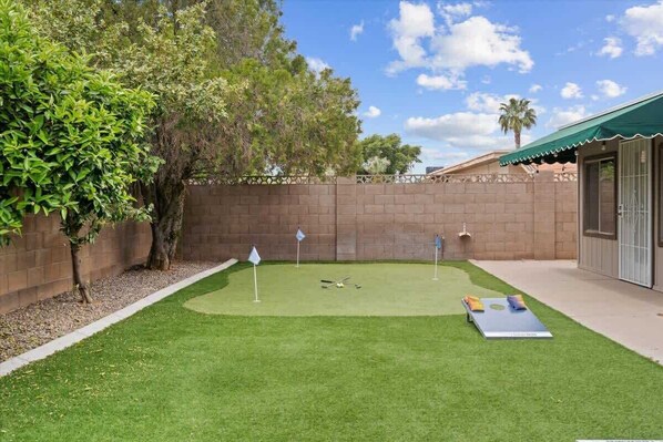 Un jardin avec un terrain d’entraînement au golf, un mur de briques et un bâtiment doté d’une marquise verte.