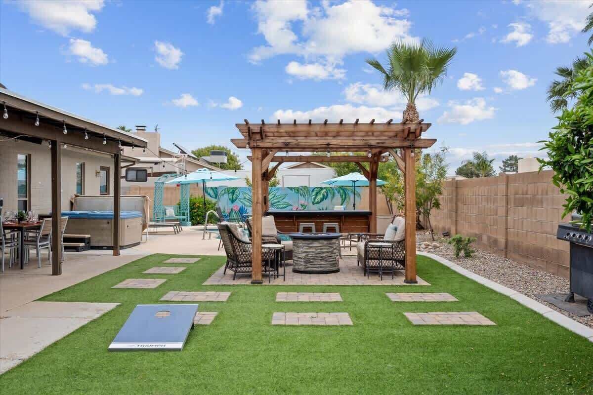 A backyard with a wooden pergola, outdoor seating, a grill, and a pool area.