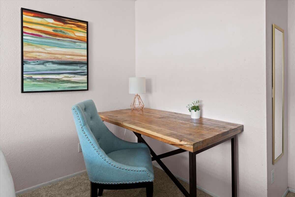 Een kamer met een houten tafel, een blauwe stoel, een wandlamp en een ingelijste afbeelding.