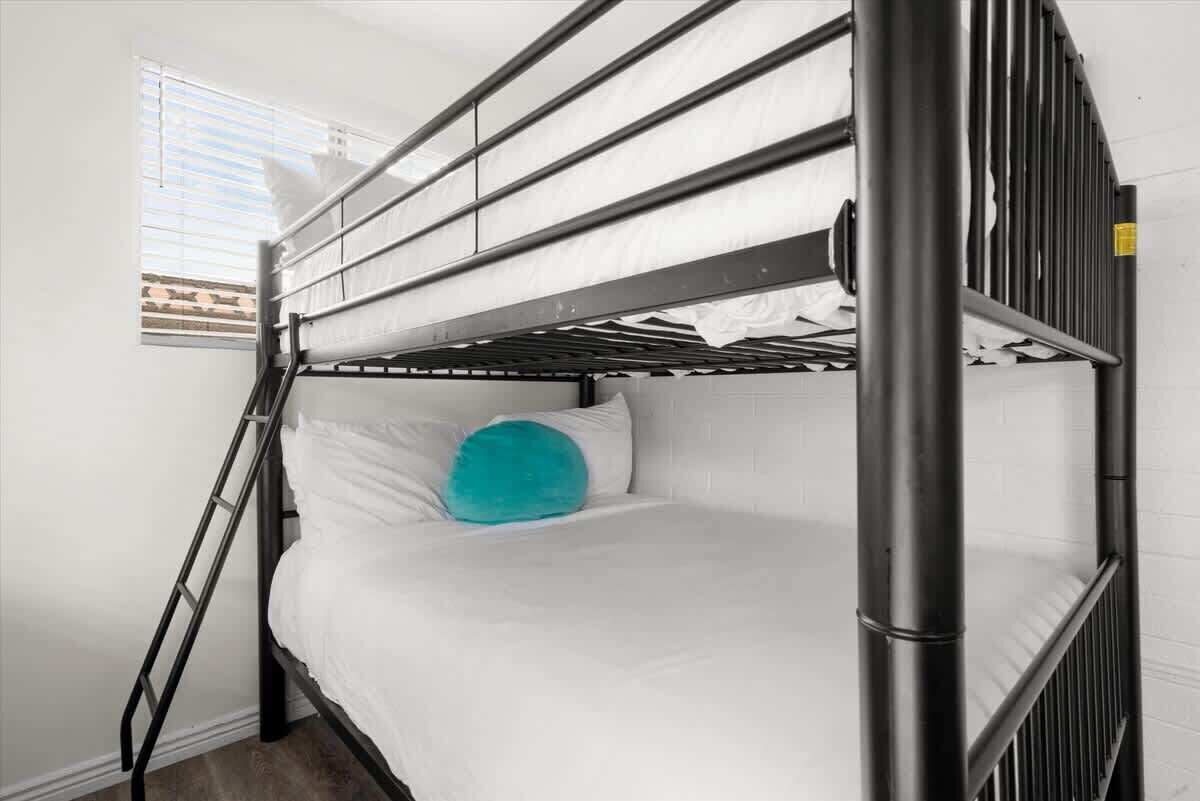 Een stapelbed met een ladder, wit beddengoed en een turquoise kussen.