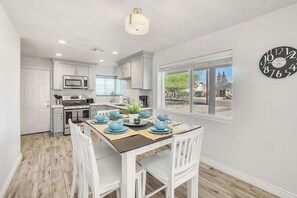 A modern kitchen with white cabinetry, a dining table set for four, and a large window providing a view of the outdoors. - Exclusive Coronado retreat: Fire pit & BBQ (Phoenix)