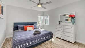 Ein Schlafzimmer mit Bett, Schminktisch, Deckenventilator und Fenster.