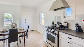 Een moderne keuken met een gasfornuis, oven en een groot raam. Er is een eethoek met een tafel en stoelen.