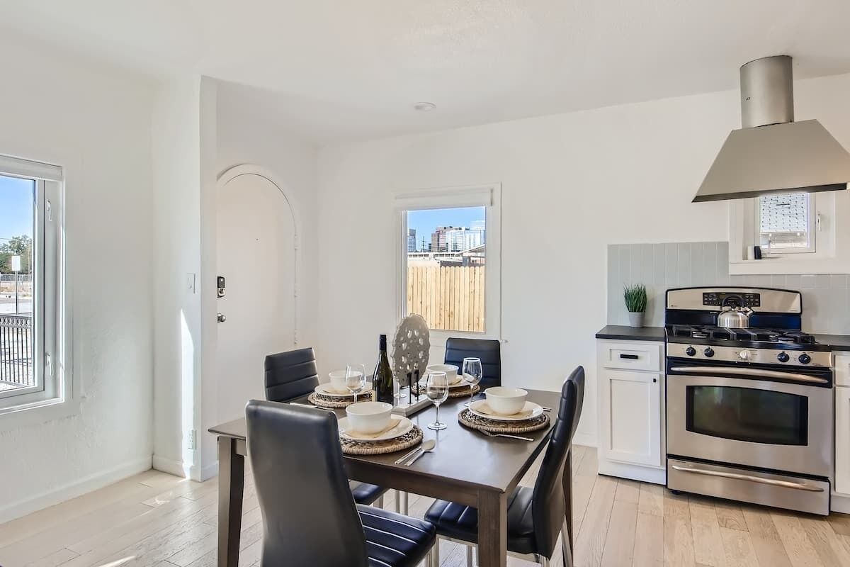 A modern kitchen with a built-in oven, a dining table set for four, and a view of the city through a window.