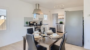 Een moderne keuken met een eethoek, voorzien van een roestvrijstalen koelkast, een inbouwoven en een hanglamp boven de tafel.