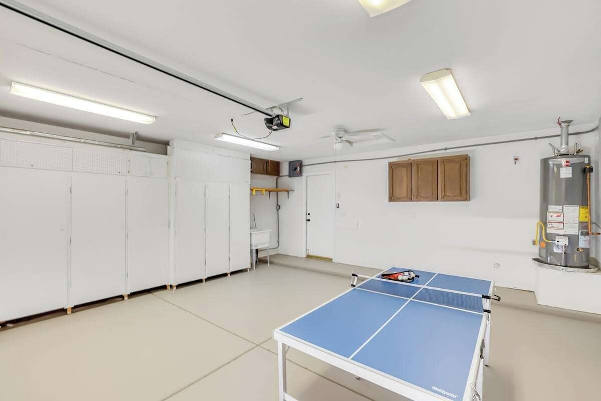 A room with a ping pong table, white lockers, a ceiling fan, and a water heater.