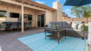 An outdoor patio area with a sofa, chairs, a table, and a TV screen. - Private pool + fire pit · Moon Valley retreat (Phoenix)