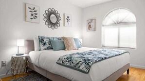 A bedroom with a bed, a nightstand, a lamp, a decorative mirror, and a window. - Private pool + fire pit · Moon Valley retreat (Phoenix)