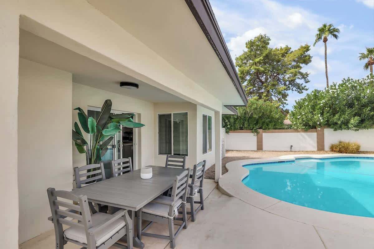 An outdoor patio with a pool, a dining table, and chairs.
