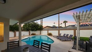 A modern outdoor pool area with lounge chairs and a table, surrounded by a low wall and vegetation. - Golf course view: pool, ping pong, fire pit (Scottsdale)
