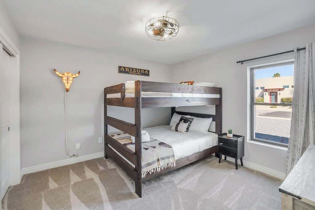 A bunk bed room with a sign on the wall, a ceiling light fixture, and a window with curtains.