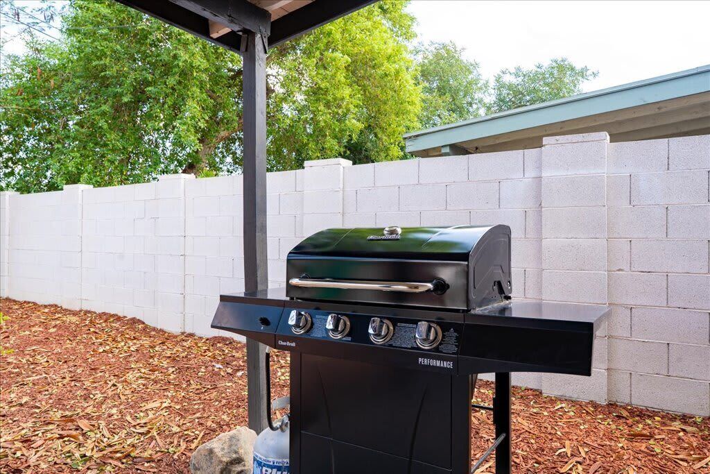A black outdoor grill with four burners and a side shelf, placed on a stand with a gas tank attached.