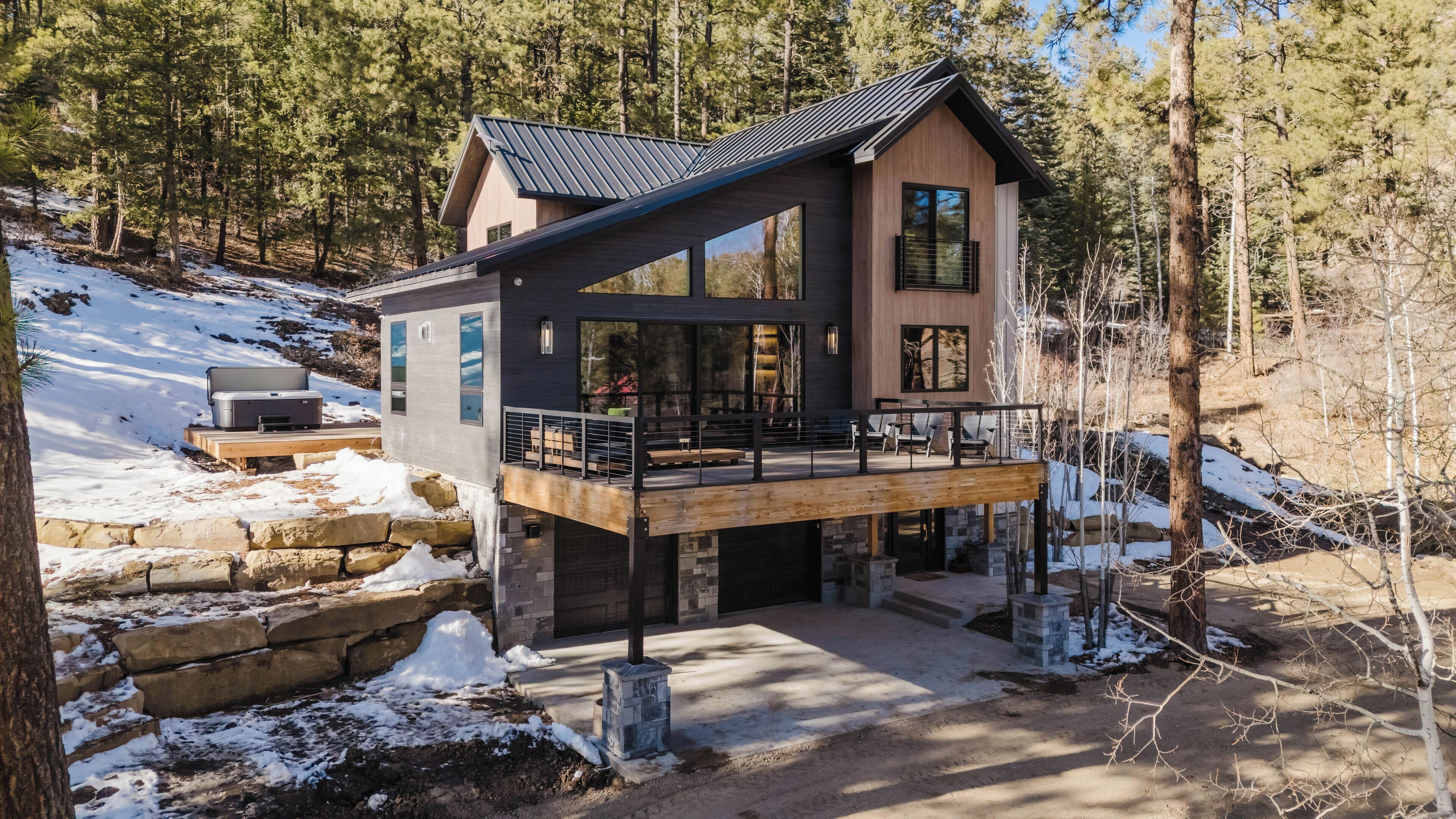 Une cabane moderne dotée d’une terrasse, entourée d’arbres et de neige.