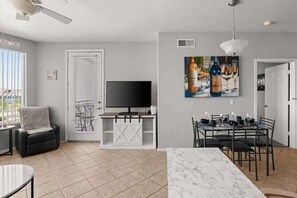 A modern living room with a TV, a dining area with a table and chairs, and a large painting on the wall. - Exclusive lakefront condo | Pool & trails (Tempe)