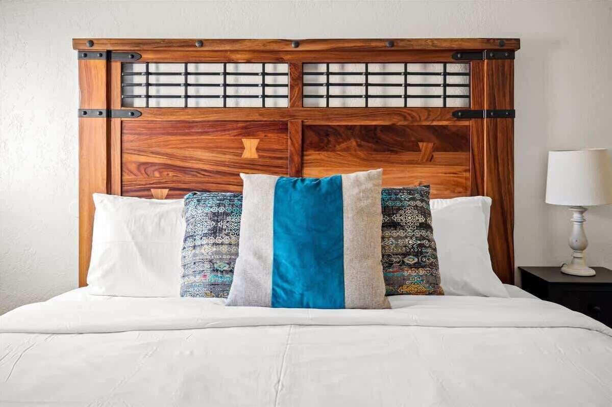 A bed with a wooden headboard, white bedding, and patterned pillows.