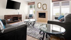 A living room with a flat-screen TV, a fireplace, two sofas, and a coffee table. - Exclusive Golf Retreat: Pool, Spa, Sleeps 18 (Phoenix)