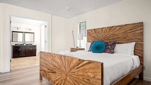 A bedroom with a wooden bed frame, white bedding, and a nightstand with a lamp. - Exclusive Golf Retreat: Pool, Spa, Sleeps 18 (Phoenix)