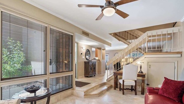 A spacious living area with a red sofa, a round table, and a ceiling fan. A staircase leads to an upper level with a balcony. - Exclusive 3BR Retreat, Pool & Spa Access (Scottsdale)