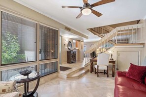 Un vaste espace de vie agrémenté d’un canapé rouge, d’une table ronde et d’un ventilateur de plafond. Un escalier mène à un niveau supérieur doté d’un balcon.