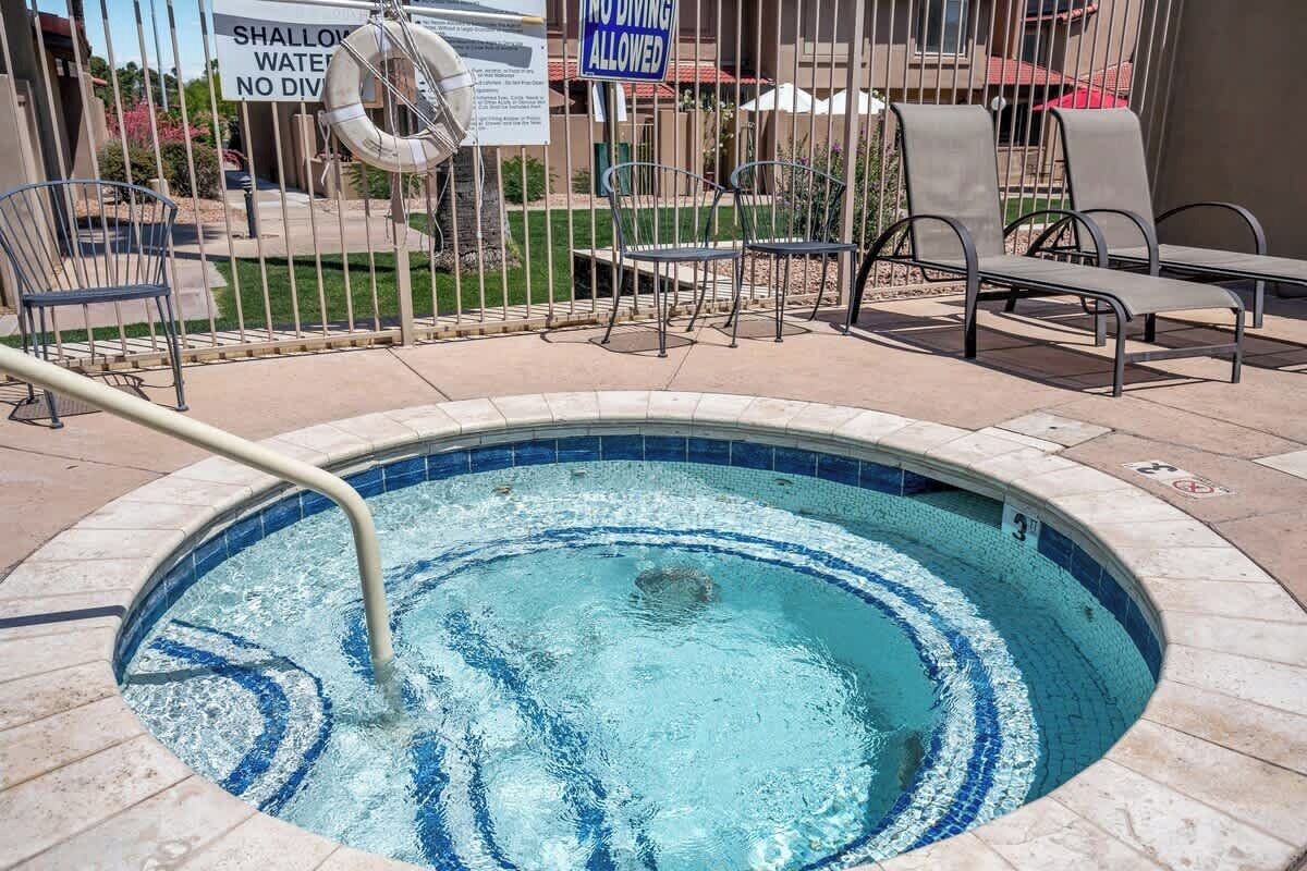 A hot tub with a metal railing, surrounded by lounge chairs and a sign prohibiting diving.