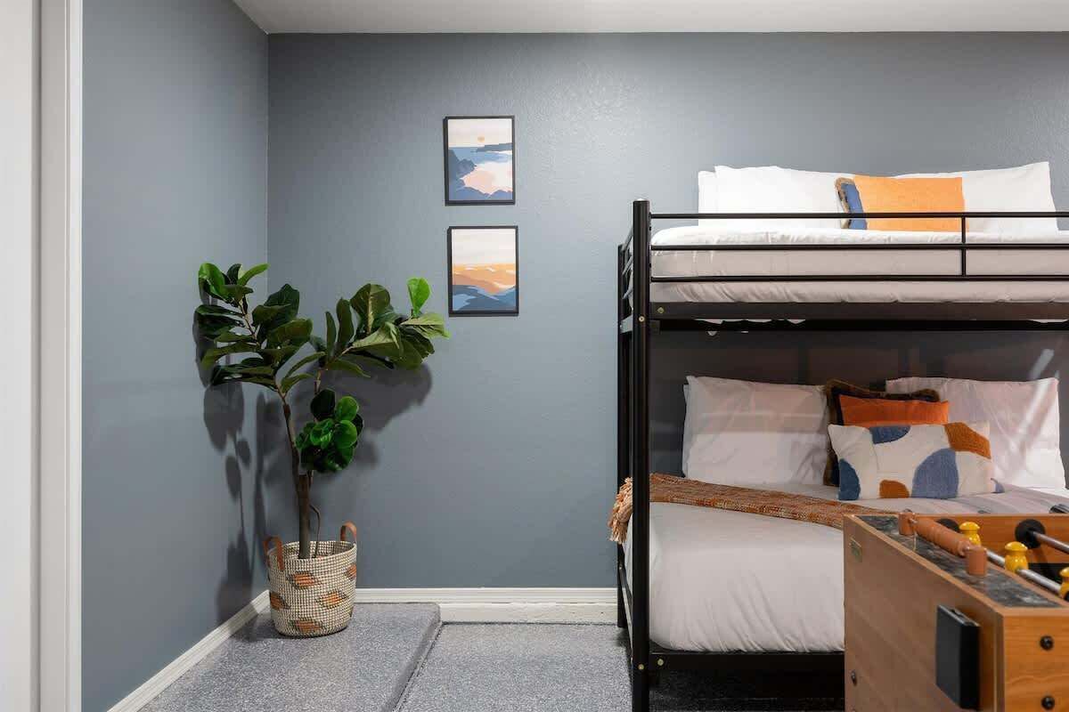 A bunk bed room with a grey wall, two framed pictures, a potted plant, and a wooden toy table.