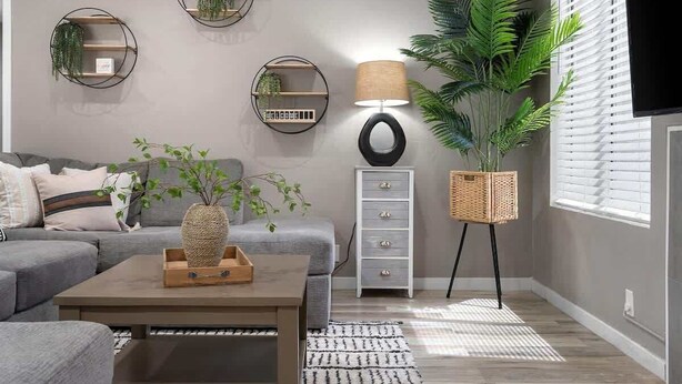 Een moderne woonkamer met een grijze bank, een salontafel, een vloerlamp en wandplanken met planten.
