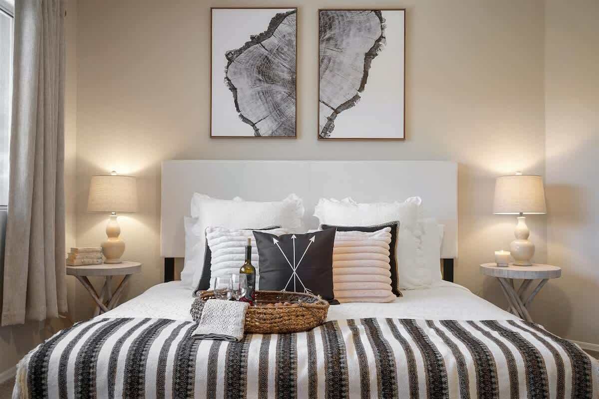 A hotel room with a large bed, two side tables with lamps, and two framed artworks on the wall.
