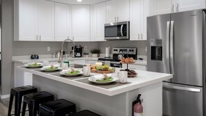 Een moderne keuken met witte kasten, roestvrijstalen apparatuur en een centraal kookeiland met ontbijtartikelen.
