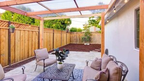 A covered patio with wooden furniture, a table, and potted plants. - Marbella Lane - Contemporary Sophisticated Home (Sunnyvale)