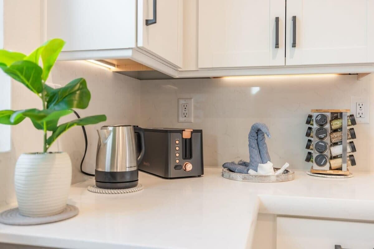A kitchen with white cabinets, a coffee maker, a toaster, a plant, and a wine rack.