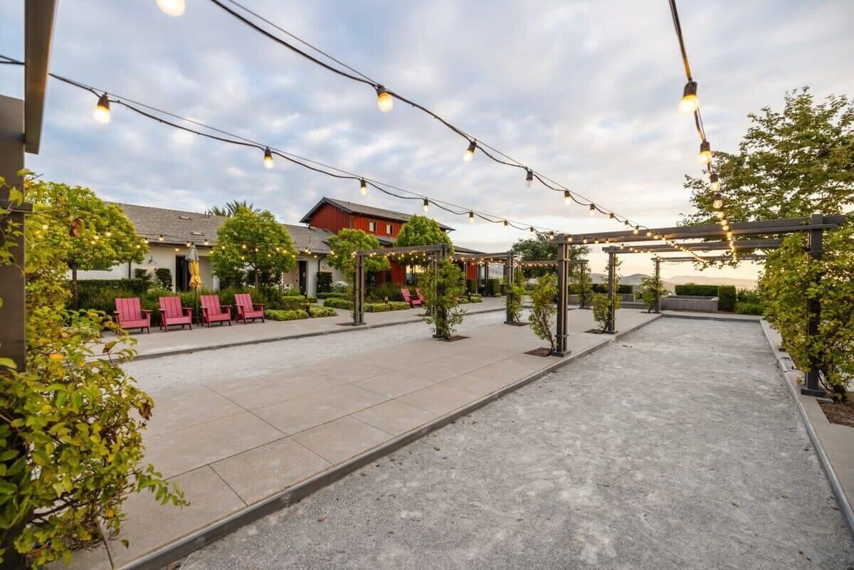 Un patio al aire libre con luces colgantes, sillas rojas y una zona de estar cubierta.