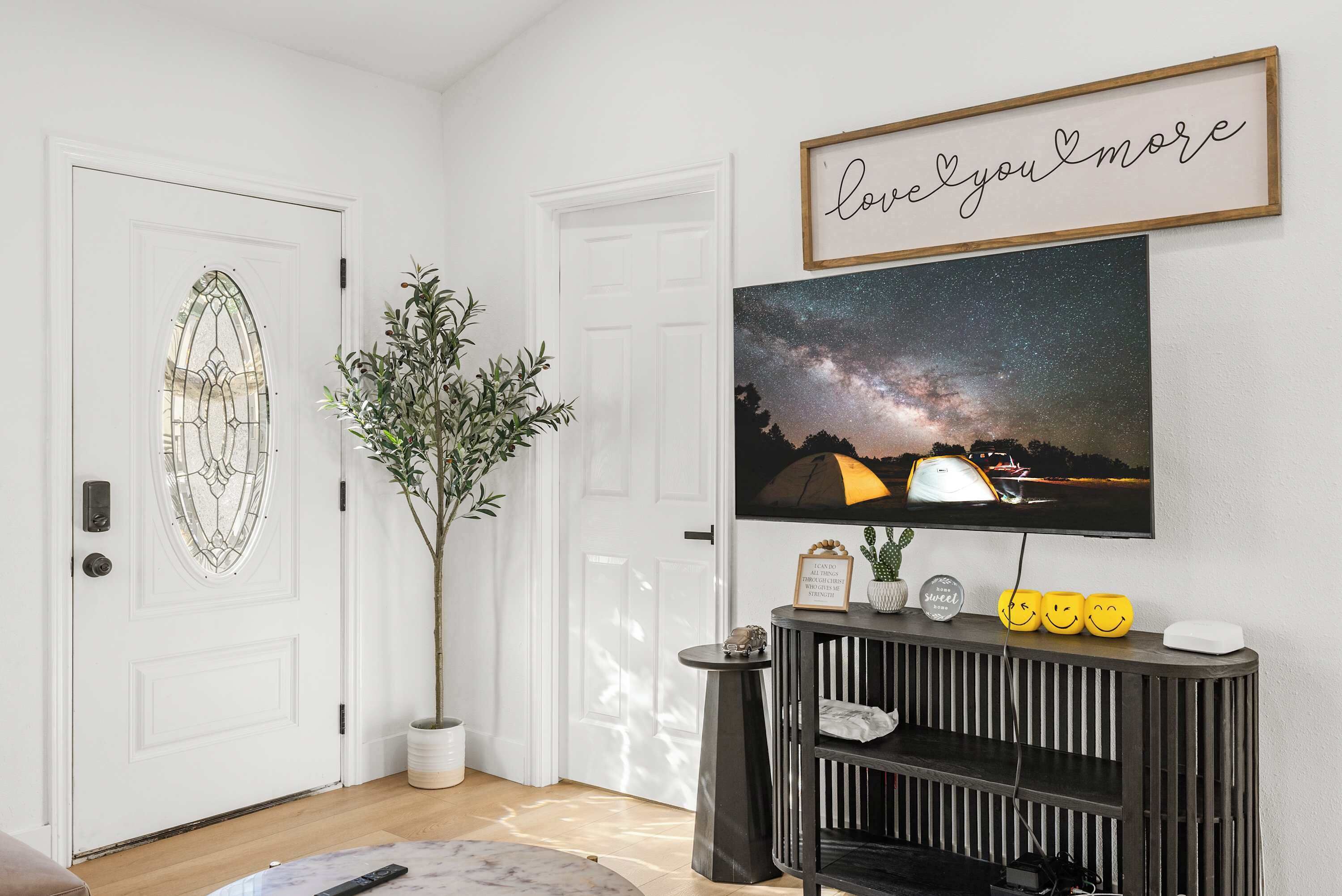 Een woonkamer met een aan de muur bevestigde televisie, een potplant en een lijst erboven.