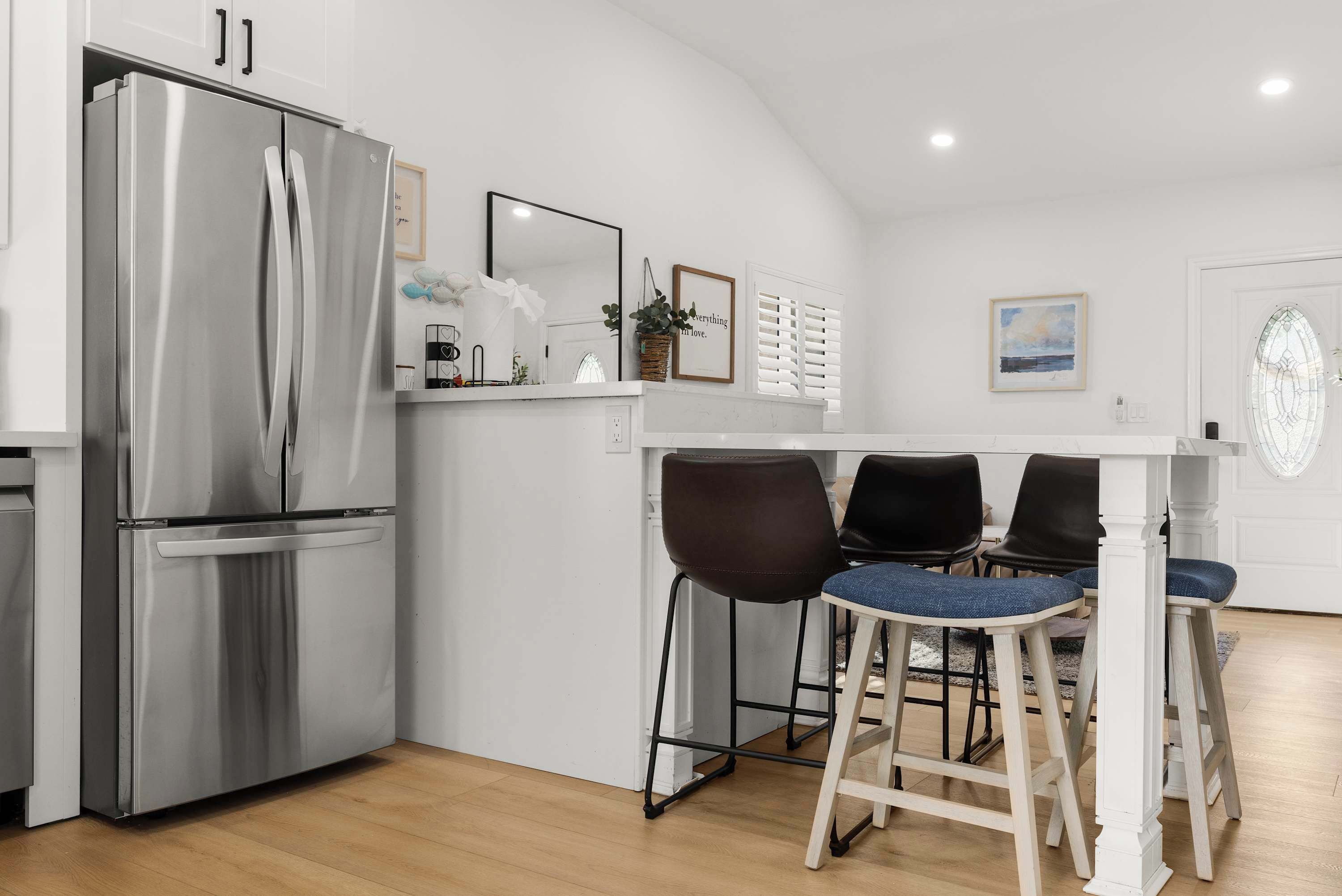 Une cuisine moderne dotée d’un réfrigérateur en acier inoxydable, d’un plan de travail blanc et d’un coin repas avec deux chaises.