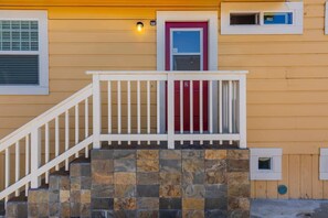 Une maison avec un escalier en pierre, une balustrade blanche, une porte rouge et une fenêtre avec des stores.