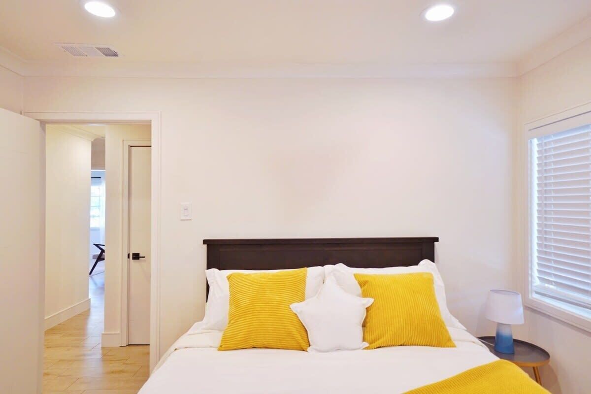 Un dormitorio con una cama, paredes blancas, cabecera de madera y una ventana con persianas.