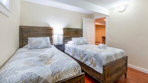 Ein Zimmer mit zwei hölzernen Betten, jeweils mit einem blumigen Bettbezug und passenden Kissen. Dazwischen befindet sich ein Nachttisch mit einer Lampe.