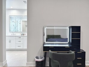 A modern bedroom with a vanity, a bed with a headboard, and a large mirror. - Marbella Lane Spacious 4BR Modern Family Home! (Placentia)